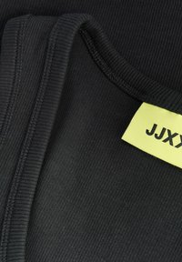 Gros plan sur un tissu côtelé noir avec des bords pliés et une étiquette de vêtement jaune montrant un texte partiel "JJX".