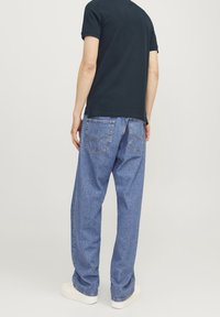 Modré denimové džíny s volným střihem, se zadními kapsami a vybledlým vzhledem. V kombinaci s tmavou košilí a bílými teniskami.