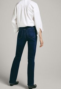 Jeans blu scuro con taglio dritto, vita media e tasche posteriori. Abbinati a una camicia bianca morbida.