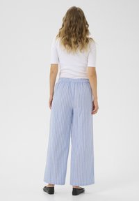 Lichtblauwe gestreepte wijde broek met een elastische tailleband, gemaakt van een zachte stof, gecombineerd met een effen wit shirt en zwarte schoenen.
