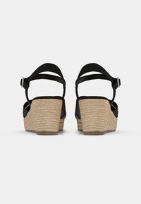 Sandales à talon compensé noires avec un talon en jute tressé, une bride de cheville ajustable et un dessus en simili cuir lisse, offrant un contraste texturé.