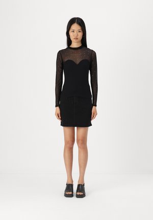 Sort langærmet bluse med gennemsigtig mesh og perleindsatser, parret med en sort denimnederdel med tætsiddende silhuet og diskrete detaljer.