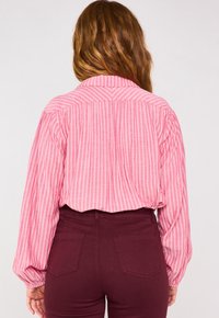 Camicia a maniche lunghe a righe rosa con colletto, caratterizzata da maniche voluminose e yoke sul retro, abbinata a jeans a vita alta color marrone.