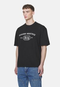 Fekete pamut póló, rövid ujjakkal és laza fazonnal. Az elejét fehér nyomtatott szöveg és minta díszíti. Egyszerű, letisztult vonalak.