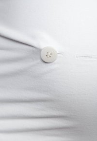 Tissu de chemise blanche tendu autour d'un bouton rond blanc cousu près d'un boutonnière horizontale.