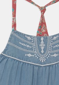 Denim-mekko sinisellä kankaalla, jossa on valkoisella brodeerattu yläosa ja punaisista kukkakuosisista olkaimista sidottu selkä.