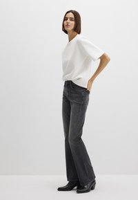 Flared black denim jeans with a faded finish, paired with a loose-fitting white shirt. Smooth texture, minimalistic design, and mid-rise waist.