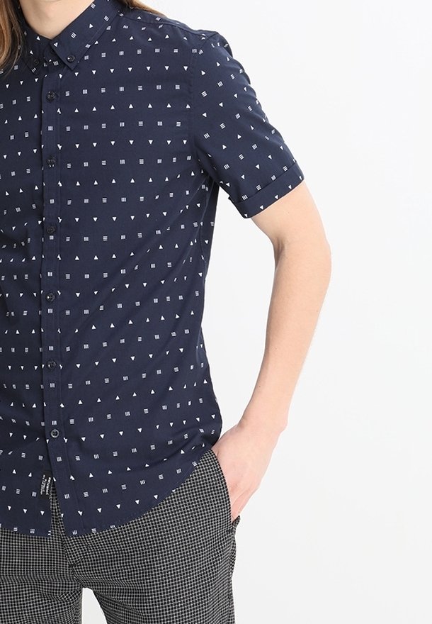 Camicetta a maniche corte, bottonata, di colore blu navy con motivi geometrici bianchi. Presenta un colletto, una tasca frontale e una vestibilità strutturata.