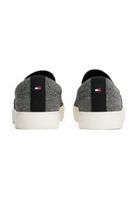 Sneakers in tessuto grigio con accenti neri e suola bianca, dotati di un piccolo logo tricolore sul retro. Design semplice slip-on.