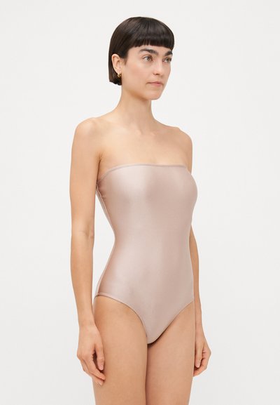Costum de baie fără bretele, într-o nuanță de roz deschis, dintr-un material satinat, cu o textură netedă, având un design cu picioare înalte și cusături minime.