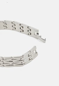 Bracelet en métal argenté avec des maillons rectangulaires et ovales entrelacés, doté d'un mécanisme de fermeture. Surface lisse avec une finition polie.
