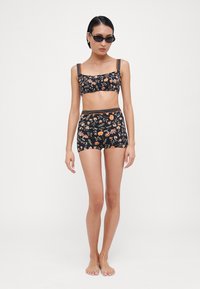 Juodas gėlių raštas, trumpas viršus ir šortai su oranžinėmis detalėmis. Yra sudėtingi gėlių raštai ir tekstūruotos petnešėlės. Lygus audinys.