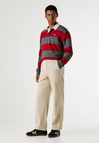 Sarkans un pelēks svītrainais garais piedurkņu polo ar baltu apkakli, papildināts ar bēšiem kordūru biksēm un melnām sporta apavām ar baltām akcentiem.