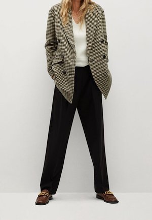 Double-breasted, houndstooth-patterned blazer in brown and black, paired with a white knit top and black wide-leg trousers. Brown loafers with gold chain.