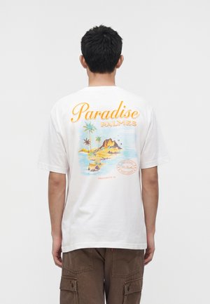 Mann mit dem Rücken zur Kamera, trägt ein weißes T-Shirt mit buntem Insel- und Palmenmotiv und dem Schriftzug „Paradise Palmes“ auf dem Rücken.