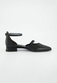 Chaussures plates en cuir noir avec un bout pointu, une sangle à la cheville ajustable et un petit talon carré. Texture lisse avec des accents minimaux.