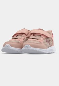 Rožiniai ir kreminiai sportiniai batai su tinklo panelėmis, lipniam užsegimui ir baltais padais. Yra mažas logotipas šone ir tekstūruotas paviršius.