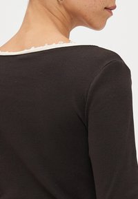 Black ribbed long-sleeve top with a rounded neckline, featuring a contrasting white scalloped trim along the neck.