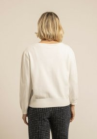 Pull blanc texturé avec un large col et un ourlet côtelé. Associe à un pantalon à carreaux sombre, vu de l'arrière.