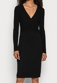 Svart ribbad långärmad klänning med djup V-ringning och åtsittande silhuett, med en jämn yta och knälång längd.