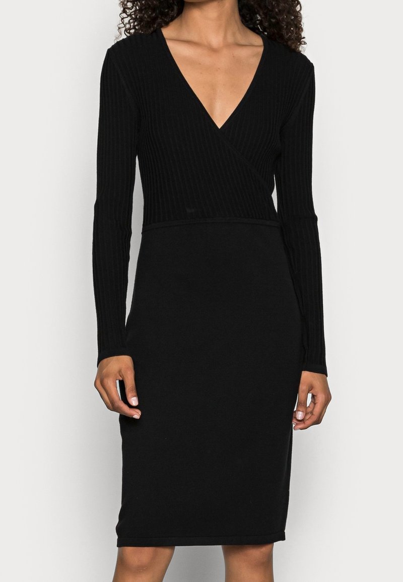 Svart ribbad långärmad klänning med djup V-ringning och åtsittande silhuett, med en jämn yta och knälång längd.