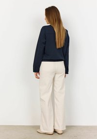 Navyblauwe top met lange mouwen en een rechte snit, gecombineerd met crèmekleurige wijde broekspijpen. Glad materiaal met een subtiele textuur. Beige schoeisel.