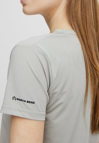 Svetlošedé športové tričko s textúrovanou tkaninou. Má krátke rukávy a čierny logotyp "North Bend" na ľavom pleci.