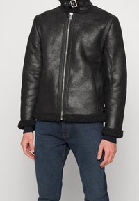 Giacca in pelle nera con collo e polsini in morbida pelliccia, dotata di cerniera frontale, texture liscia e design elegante.