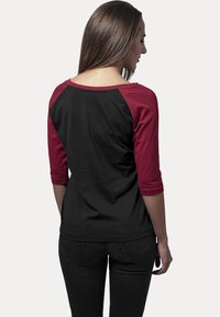 Svart og maroon trekvart ermelang raglan-skjorte med rund hals og myk stoff; glatt tekstur med kontrasterende farge på ermene.