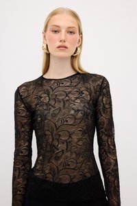 Top a maniche lunghe in pizzo nero con intricati motivi floreali e paisley, texture trasparente e orlo nero solido in vita.