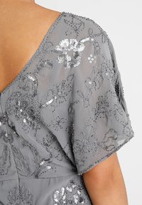 Szary półprzezroczysty materiał z haftem kwiatowym z srebrnymi cekinami na krótkich rękawach i górnej części pleców odzieży.