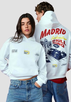 Zwei Models tragen weiße Racing-Hoodies mit Red Bull Racing-Logos; eines zeigt die Vorderseite, das andere die Grafik Madrid 2026 mit Rennwagen auf dem Rücken.