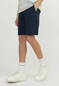 Shorts bleu marine en tissu texturé, avec des poches latérales et une coupe décontractée, associés à des baskets blanches et des chaussettes.