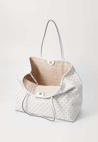 Sac fourre-tout blanc Guess avec motif géométrique, ouverture supérieure dévoilant une doublure intérieure beige avec impression répétée du logo et fermeture par bouton magnétique.
