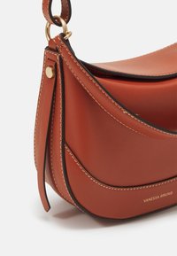 Bruine leren handtas met een gebogen ontwerp, contrasterende zwarte stiksels, gouden hardware accenten en een schouderband.