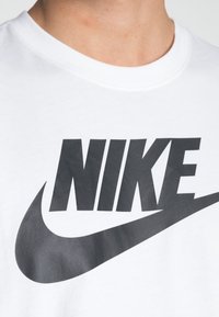 Hvit bomull T-skjorte med en stor svart Nike-logo og swoosh på fronten; rund hals og korte ermer. Glatt tekstur.
