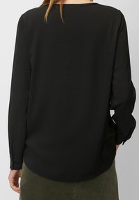 Schwarze Bluse mit langen Ärmeln und rundem Ausschnitt, glatter Textur und abgerundetem Saum. Verfügt über geknöpfte Manschetten und ein fließendes Design.