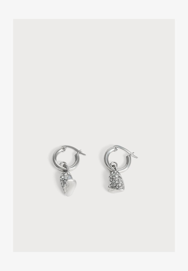 Boucles d’oreilles créoles en argent avec pendentifs en forme de cœur ; un pendentif est lisse, l’autre est recouvert de petits strass transparents.