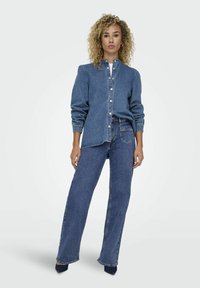 Denim skjorte med knapper og højtaljede brede bukser i en mellemblå farve. Skjorten har en mandarin-krave og opfoldede ærmer; bukserne har baglommer.
