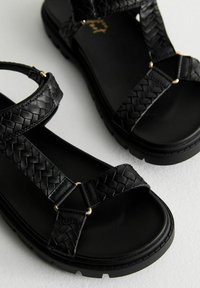 Zwarte geweven sandalen met textuurbanden en gouden accenten. Beschikt over een platte zool en een minimalistisch ontwerp. Geschikt voor casual gebruik.