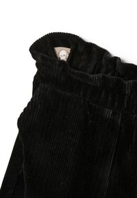 Zwarte corduroy broek met een gestructureerd ribbeloppervlak, voorzien van een elastische tailleband en een klein label binnenin.