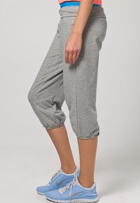Pantaloni sportivi grigi a cropped con polsini elasticizzati, dotati di una comoda cintura, abbinati a scarpe da ginnastica azzurre chiare.