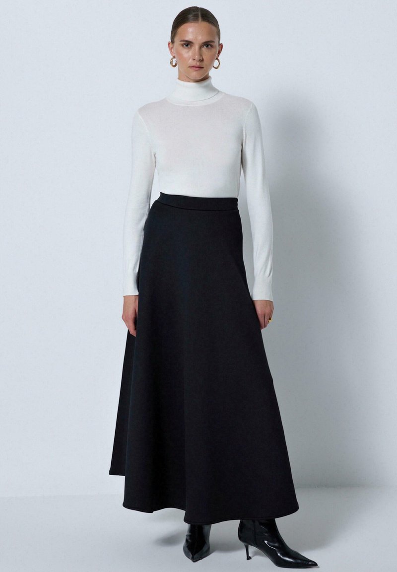 White turtleneck top paired with a black, floor-length skirt. The skirt features a smooth texture and a fitted waistband. Black stiletto boots.