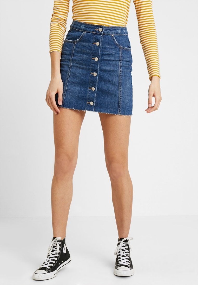 Jeansminikjol med knapprad framtill, lätt fransad fåll, två framfickor och en figurnära silhuett. Bärs med svarta sneakers med hög krage.