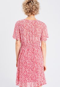 Abito rosso a fiori con maniche corte e arricciate. Presenta una vita arricciata, un tessuto leggero e una texture trasparente e fluida con motivi di fiori bianchi.