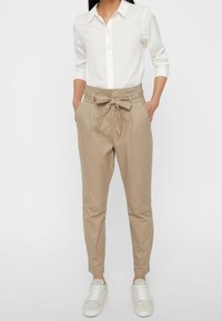 Light beige tapered pants with a tied waistband, paired with a white long-sleeve button-up shirt and white sneakers.