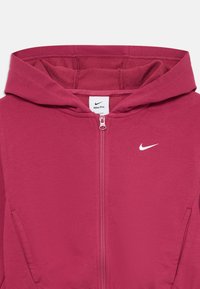 Ružičasta zip-up dukserica s prednjim zatvaračem, kenguruzim džepovima i malim Nike logoom na lijevoj strani grudi. Izrađena od meke, teksturirane tkanine.