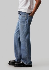 Jeans a gamba larga blu in denim con un lavaggio medio, caratterizzati da una tasca frontale e una vestibilità rilassata, abbinati a scarpe con plateau nere.