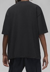 Czarna, oversize koszulka z bawełny z krótkimi rękawami, okrągłym dekoltem i gładkim tyłem. Posiada luźny krój i miękką teksturę.