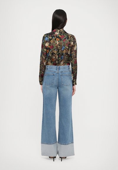 Sheer black floral blouse with long sleeves, paired with light blue high-waisted wide-leg jeans featuring a contrasting gray hem.